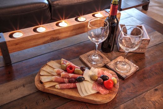 Red wine with Charcuterie board on rustic wood with candles behind a spread of prosciutto panino, mozzarella cheese, Genoa salami, Fontina cheese and artisanal crackers.