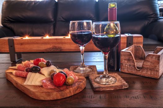 Red wine with Charcuterie board on rustic wood with candles behind a spread of prosciutto panino, mozzarella cheese, Genoa salami, Fontina cheese and artisanal crackers.