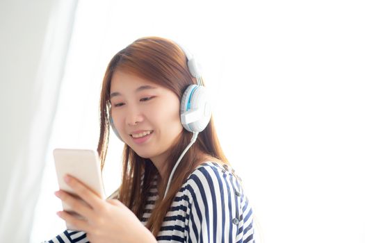 Beautiful asian young woman enjoy listen music with headphone and holding smart mobile phone while sitting in bedroom, relax girl with earphone, leisure and technology concept.