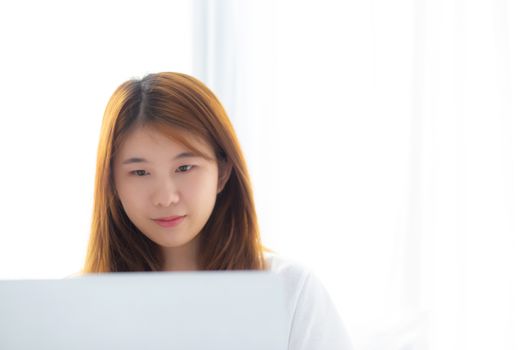 Portrait of beautiful asian young woman setting on bed using laptop computer at bedroom for leisure and relax, freelance with girl working notebook, communication and lifestyle concept.