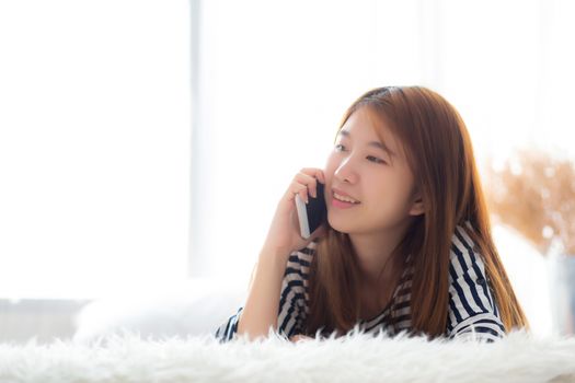 Beautiful young asian woman smiling lying relax on the bed in the morning, girl using mobile smart phone talking enjoy, communication and social network concept.