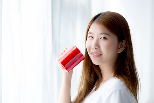 Beautiful of portrait young asian woman with drink acup of coffee standing curtain window background in bedroom, girl relax in morning at home, lifestyle concept.