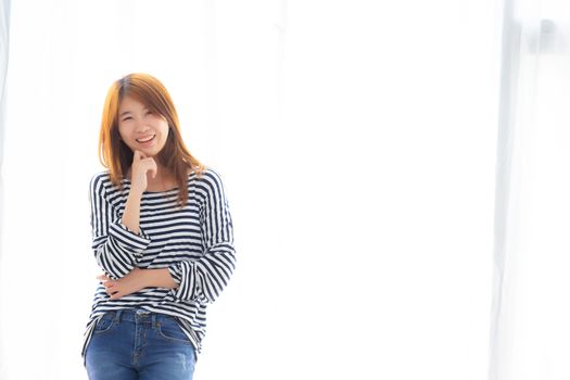 Portrait of beautiful young asian woman standing the window and smile while wake up with sunrise at morning, lifestyle and relax concept.