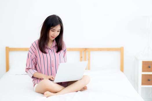 Portrait of beautiful asian young woman setting on bed using laptop computer at bedroom for leisure and relax, freelance with girl working notebook, communication and lifestyle concept.