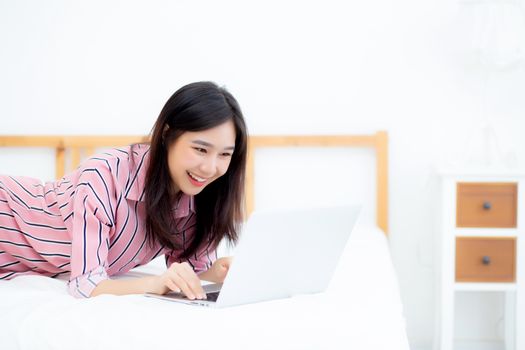 Beautiful asian young woman lying on bed using laptop at bedroom for leisure and relax, freelance with girl working notebook, communication concept.