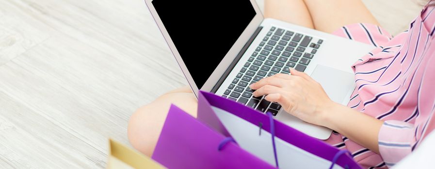 Banner website closeup asian woman shopping online with laptop computer sitting on floor on room, girl holding credit card purchase and shopping bags, lifestyle concept.