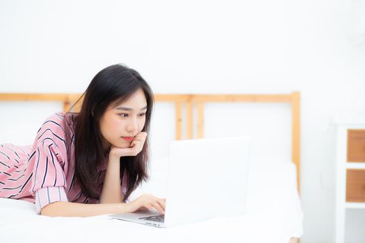 Beautiful asian young woman lying on bed using laptop at bedroom for leisure and relax, freelance with girl working notebook, communication concept.