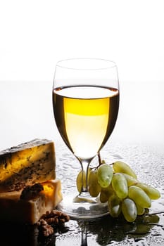 Glass of wine, pieces of cheese and bunch of grape on a glass background with waterdrops