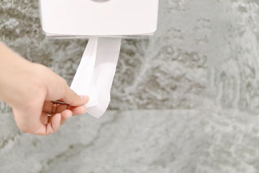 Closeup woman hand picking a white tissue from tissue roll in the restroom.