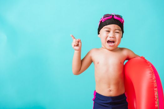 Summer vacation concept, Portrait Asian happy cute little child boy wear goggles and swimsuit hold watermelon inflatable ring, Kid having fun on summer vacation, studio shot isolated blue background