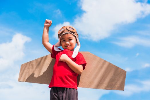 Happy Asian funny child or kid little boy smile wear pilot hat and goggles play toy cardboard airplane wing flying raises hand up against summer blue sky cloud background, Startup freedom concept