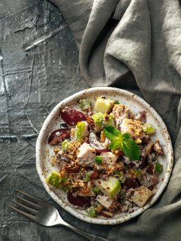 Waldorf salad, copy space. American fruit and nut salad with apples, celery, grapes, chicken meat, dressed mayonnaise. Craft plate with ready-to-eat waldorf salad on gray background. Topview. Vertical