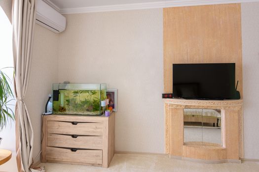 A corner in the room, there is an aquarium, an air conditioner hangs and a stylized place for a TV