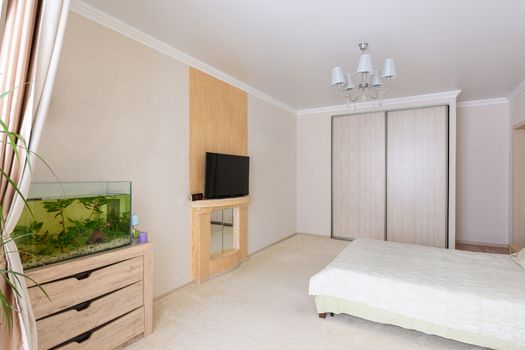 Interior of a spacious bedroom, stands an aquarium, TV and wardrobe