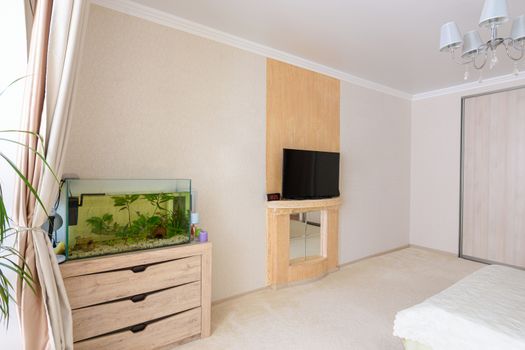 A fragment of the bedroom interior, a view of the wall opposite the bed, there is an aquarium against the wall and a TV hanging