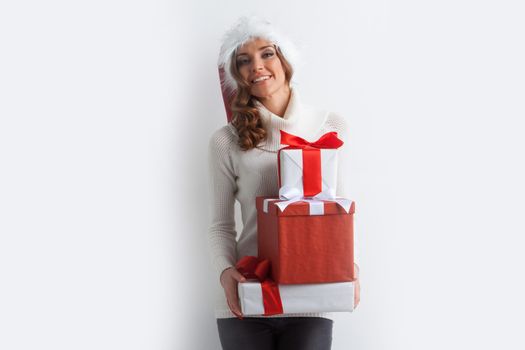 Festive blonde woman in Santa hat holding pile of Christmas gifts on white background