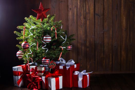 Decorated Christmas tree with candy canes , star , striped baubles and gift boxes on wooden background