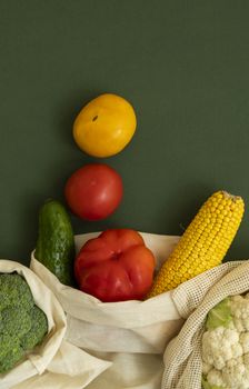 Vegetables in eco bag on green surface. Pepper, tomato, corn, cucumber, broccoli, cauliflower in reusable shopping eco friendly cotton fabric bags. Zero waste and plastic free concept. Sustainable