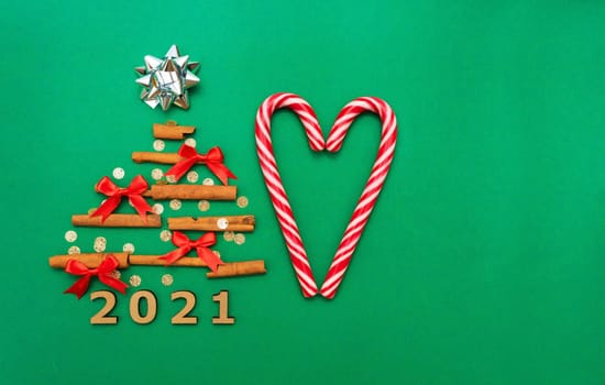 Christmas composition 2021 cinnamon tree, red bows, candy, Christmas cane candies on a green background. Christmas, winter, new year concept. Flat lay, top view, copy space