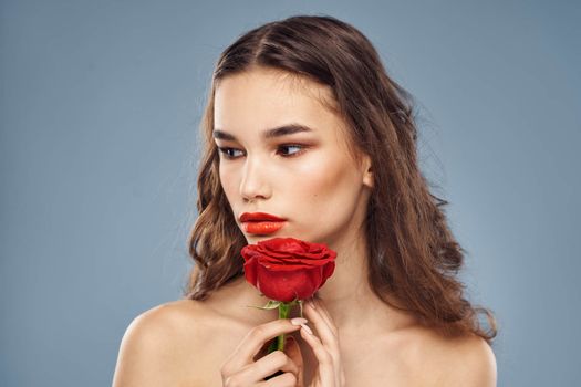 Woman portrait with red rose near the face on gray background and makeup curly hair. High quality photo