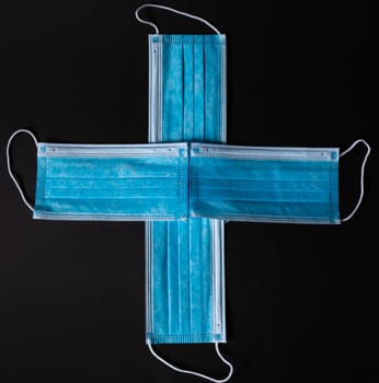 Four surgical face masks put together as a cross in black background