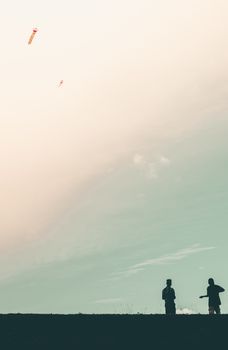 Silhouette of two boys flying kites on a river bank in the evening