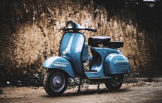 Vintage light blueish scooter bike against dirt wall