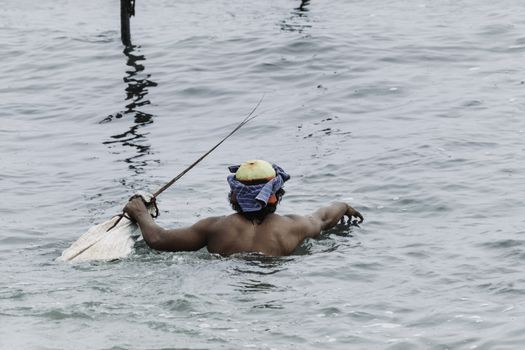 Stilt fisherman in Sri Lanka swimming to his stilt pole and kithul stick in his hands