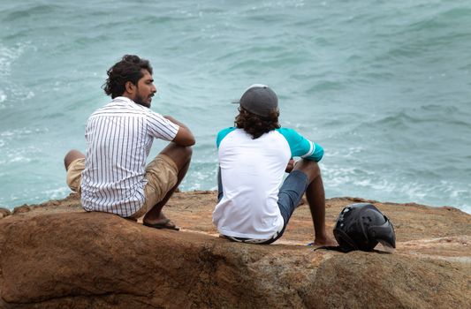 Best friends having a casual conversation on a rock on the beach relaxing.