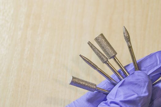 Set of milling cutters in a manicurist hand on wood background and some free space for text. Manicure and pedicure professional tools.