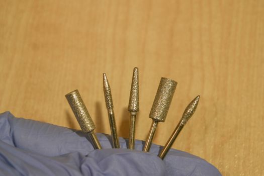 Set of milling cutters in a manicurist hand on wood background. Manicure and pedicure professional tools.