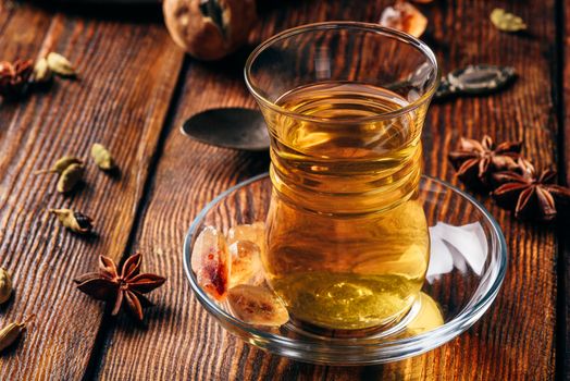 Spiced tea with star anise, cardamom and dried lime in armudu glass over wooden surface