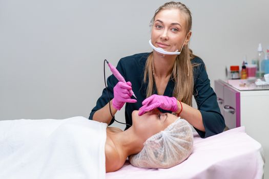 Cosmetology cabinet client lies on couch. Beautician applies permanent ink on lips. Procedure of permanent lip makeup. Free space. Beauty industry