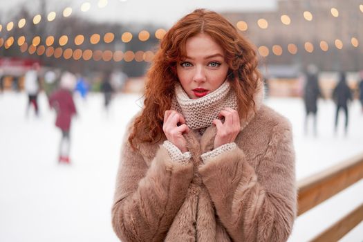 Young beautiful redhead girl freckles ice rink background Pretty woman curly hair portrait walking new year fair Modern cute female drink hot beverage mulled wine chrismas holiday decorated street.