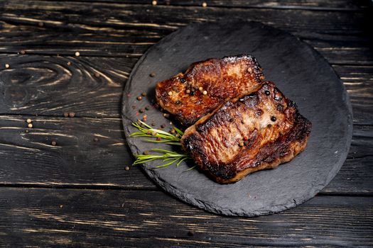 A juicy piece of fried meat lies on a stone plate against a black wooden table. Degree of roasting well done. Food concept with copy space