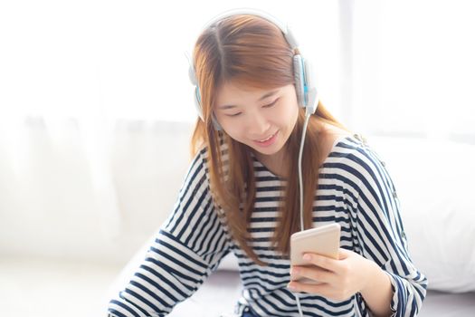 Beautiful asian young woman enjoy listen music with headphone and holding smart mobile phone while sitting in bedroom, relax girl with earphone, leisure and technology concept.