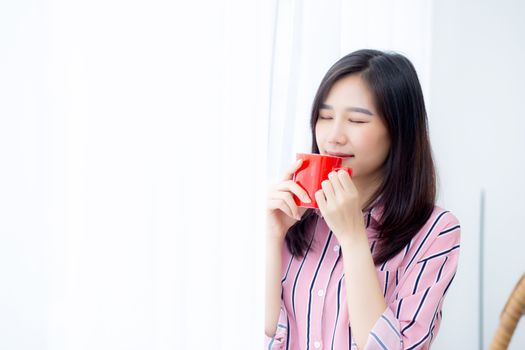 Beautiful of portrait young asian woman with drink a cup of coffee standing curtain window background in bedroom, girl relax in morning at home, lifestyle concept.