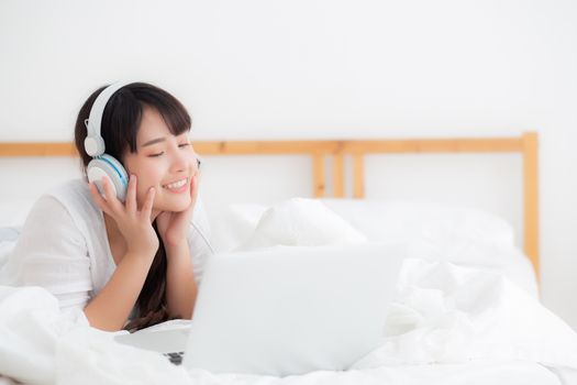 Beautiful young asia woman lying in bedroom using laptop computer showing video call chat at home, girl greet and listen and talking messenger, communication and lifestyle concept.