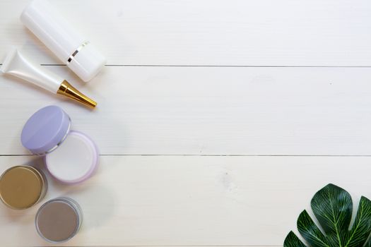 cosmetic and skin care product and green leaves on white wood table, beauty with treatment cream and moisturizing on wooden desk, health and wellness concept, top view.