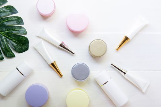 cosmetic and skin care product and green leaves on white wood table, beauty with treatment cream and moisturizing on wooden desk, health and wellness concept, top view.
