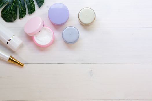 cosmetic and skin care product and green leaves on white wood table, beauty with treatment cream and moisturizing on wooden desk, health and wellness concept, top view.