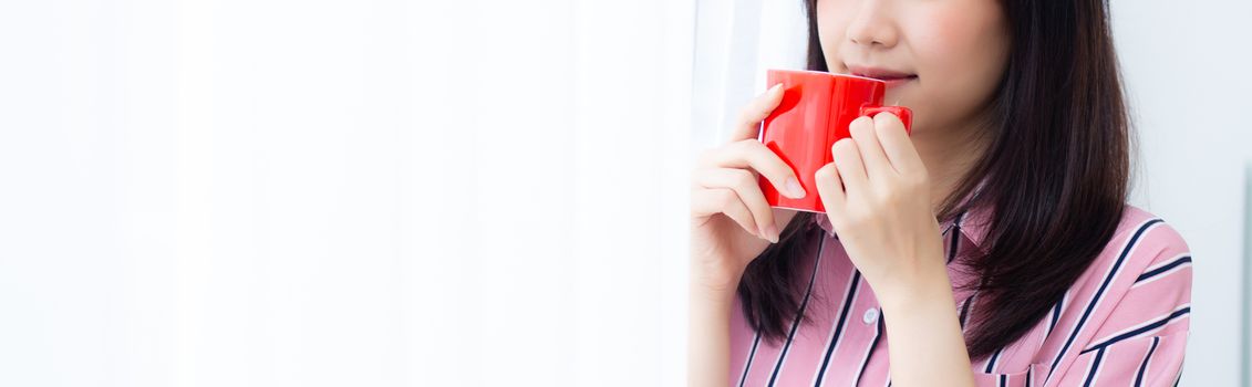 Closeup young asian woman with drink a cup of coffee standing curtain window background in bedroom, girl relax in morning at home, lifestyle concept.