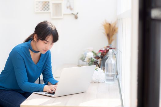 Beautiful portrait asia young woman working online on laptop sitting at cafe shop, professional female freelance using notebook computer, business and communication concept.