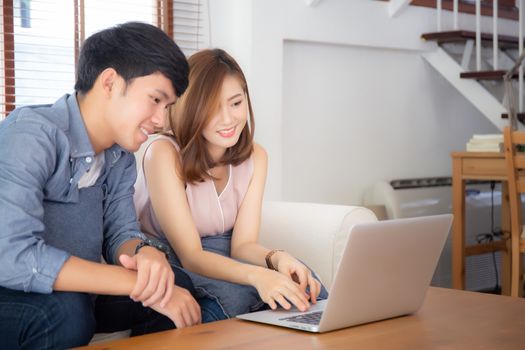 Asian young couple using laptop computer think and searching internet together, man and woman casual smiling work at home with happy and relax, communication and business concept.