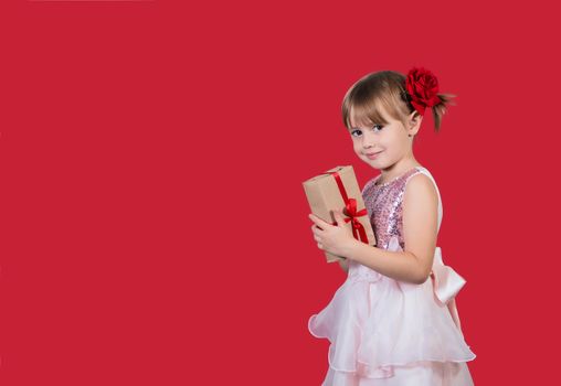 Beautiful cute cacusian little girl in an elegant dress and with a rose pin in her hair holding a gift and smiling. Merry Christmas or Valentine's Day presents shopping sale.