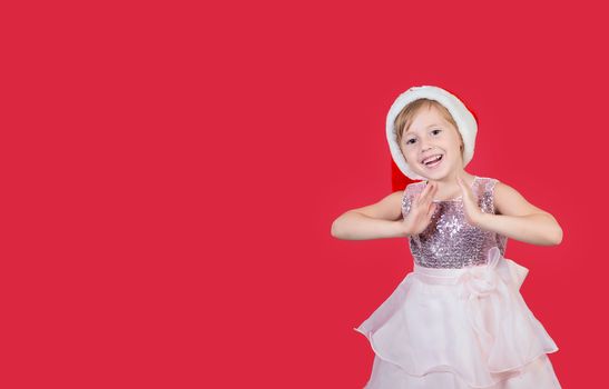 Adorable funny cacusian little girl in santa hat claps his hands for a gift celebrating happy New Year isolated on red background. Merry Christmas presents shopping sale.