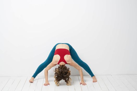 sports woman in a bright room doing yoga in full growth blue leggings and a red tank top. High quality photo