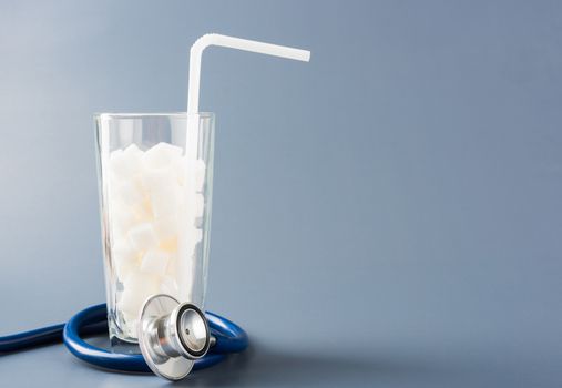 A glass full of white sugar cube sweet food ingredient and doctor stethoscope, studio shot isolated gray background, health high blood risk of diabetes and calorie intake concept and unhealthy drink