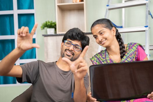 Young Indian couple busy in planning home improvement or renovation by looking into laptop while sitting together at unfinished apartment