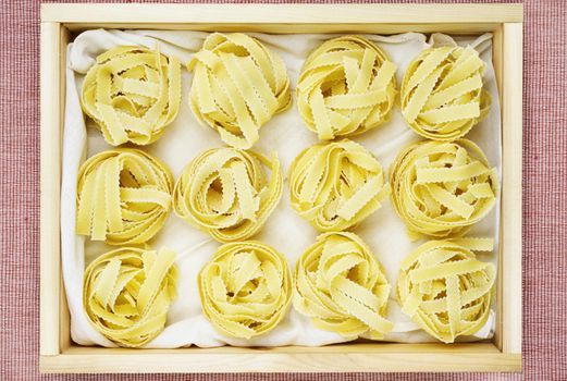 Beautiful nests of Italian pasta  fettuccine on white cotton cloth  in wooden box  , thin ribbons of pasta with geometrical edges and rough surface